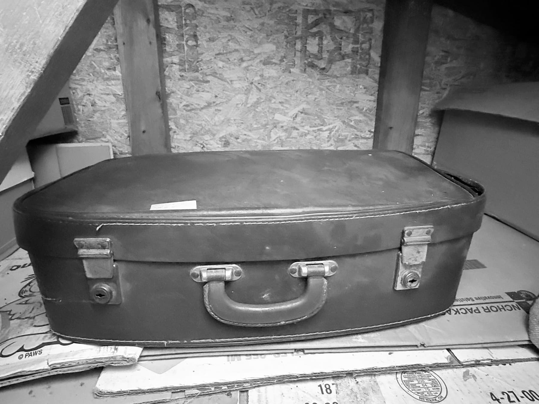 An old leather suitcase resting on cardboard boxes in an attic
